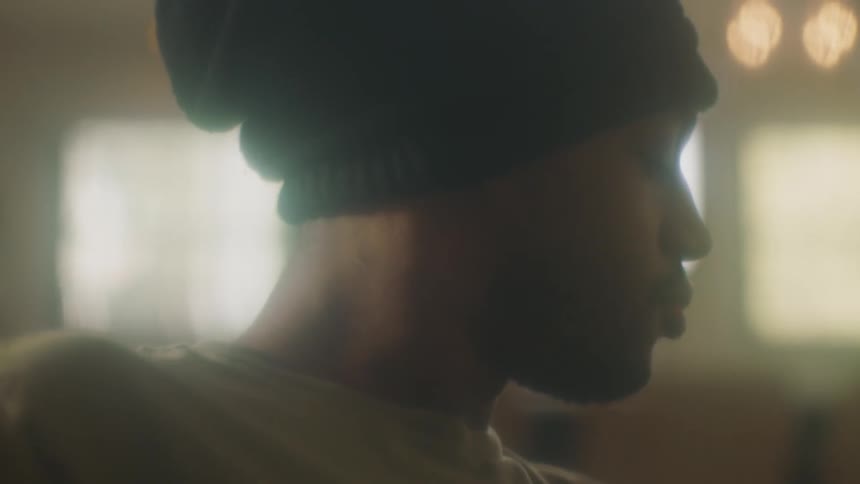 A man with a hat in a room with a wall and window in the background