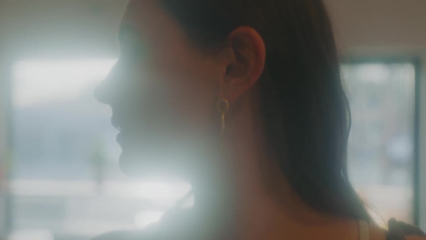 A woman stands in front of a large window at home and looks worried as she looks to the side of her