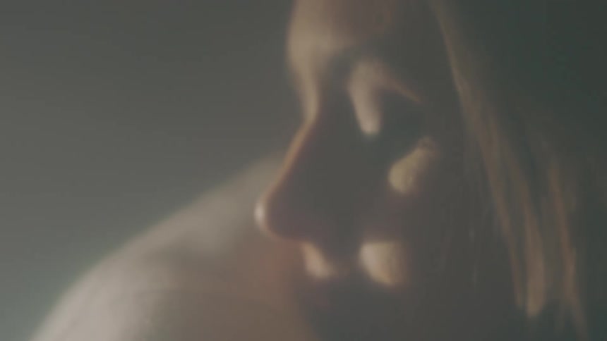 Woman hugging a man reclines her head on his shoulder inside a dimly lit room
