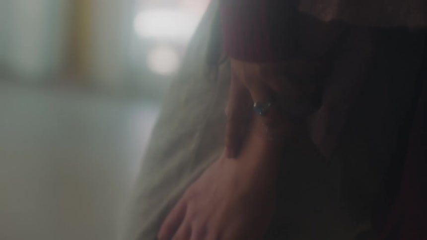 A person with a ring holding the wrist of another person in a room with a wall in the background