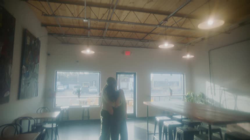 A couple hug as they stand in the middle of an empty cafe