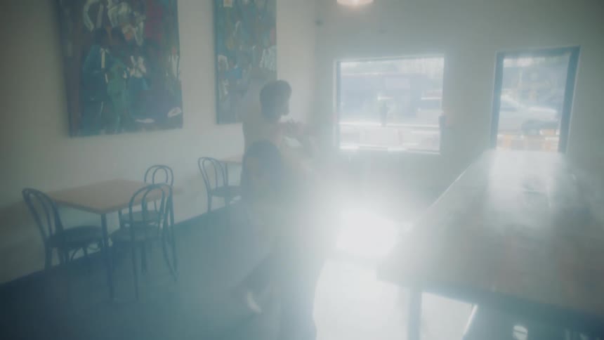 A man and woman perform a modern dance around a long wood table in an empty cafe