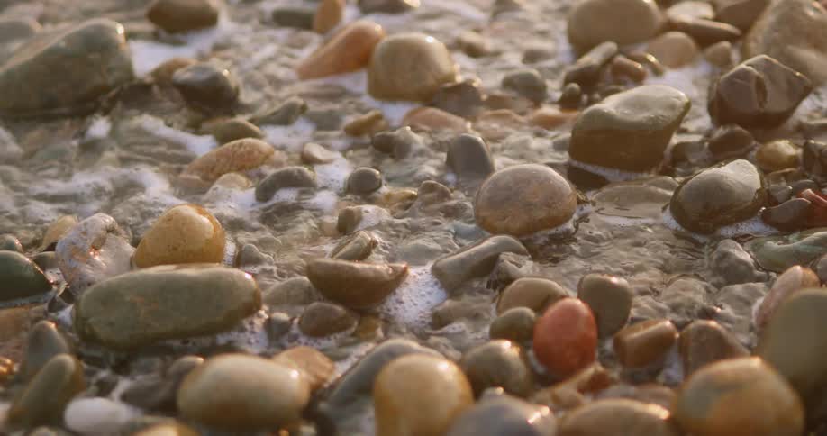 Foaming ocean water flows off pebble strewn beach
