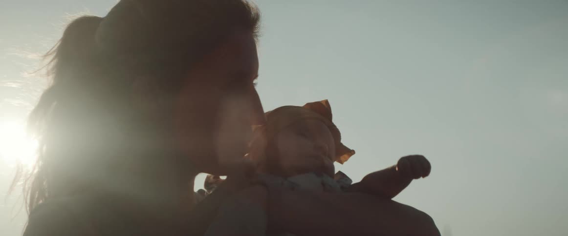 The sun shines and glares behind a mom holding and kissing her baby daughter