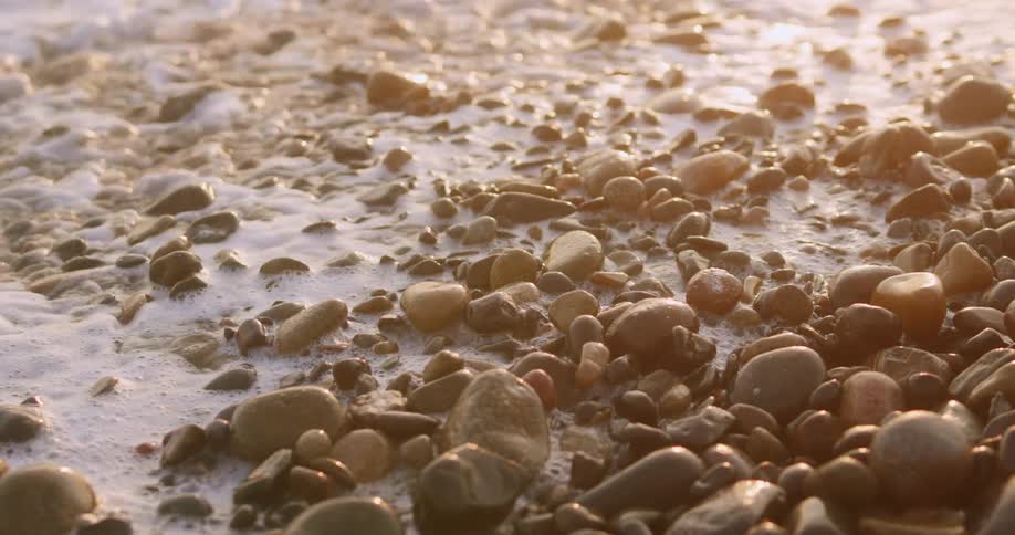 White foam waves cover smooth stones on shore before receding