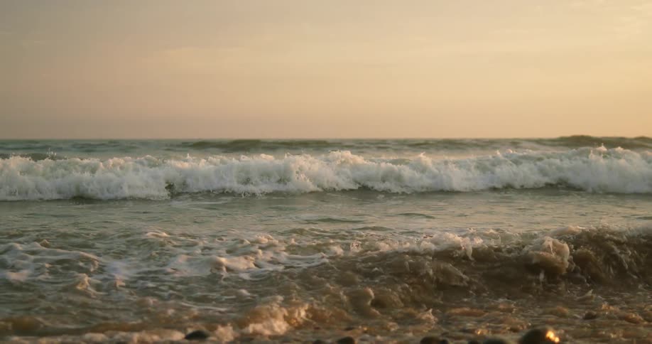 Ocean waves gently crashing on the coast of a beach at sunset