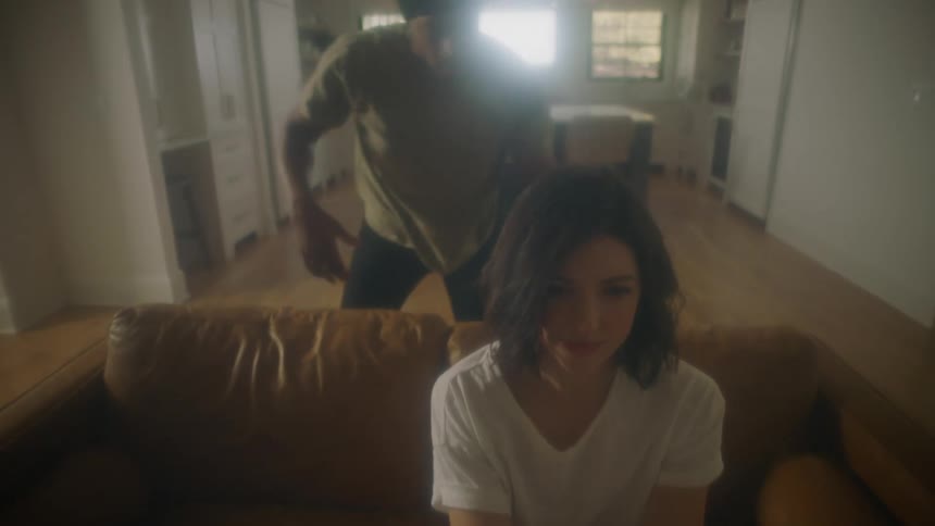 A man dances around his couch and massages his wifes back before she joins in dancing