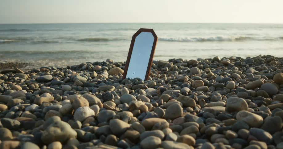 Mirror set among pebbles on beach reflects blue sky