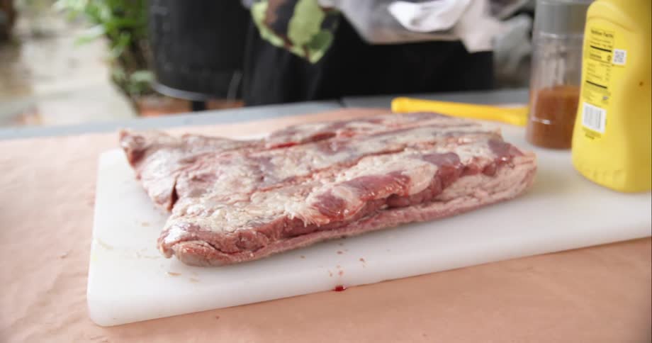 A person who is preparing a large slab of meat on a cutting board pass it dry with a paper towel