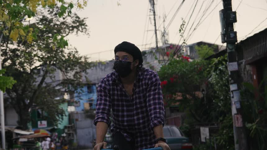 A man wearing a face mask pedals on his bicycle down a neighborhood street