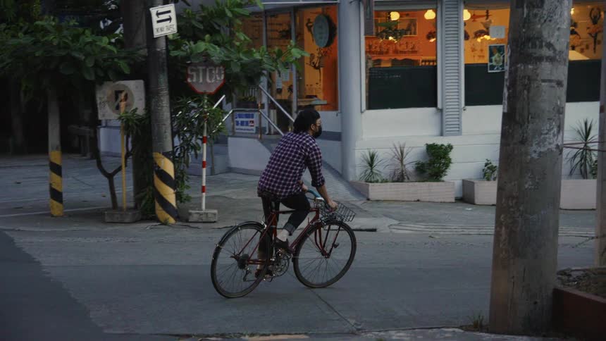 A man wearing a mask and cap riding a bicycle turns a corner on a street