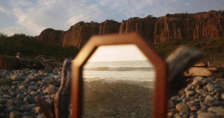 Ocean waves next to a beach refelcted on a mirror standing near the cliffs at sunset