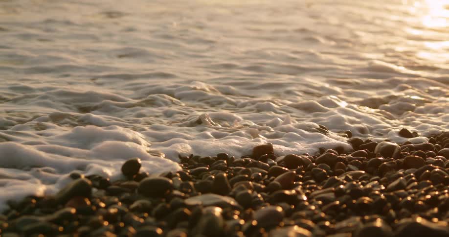 Ocean waves gently crashing over the small pebbles in the coast at sunset