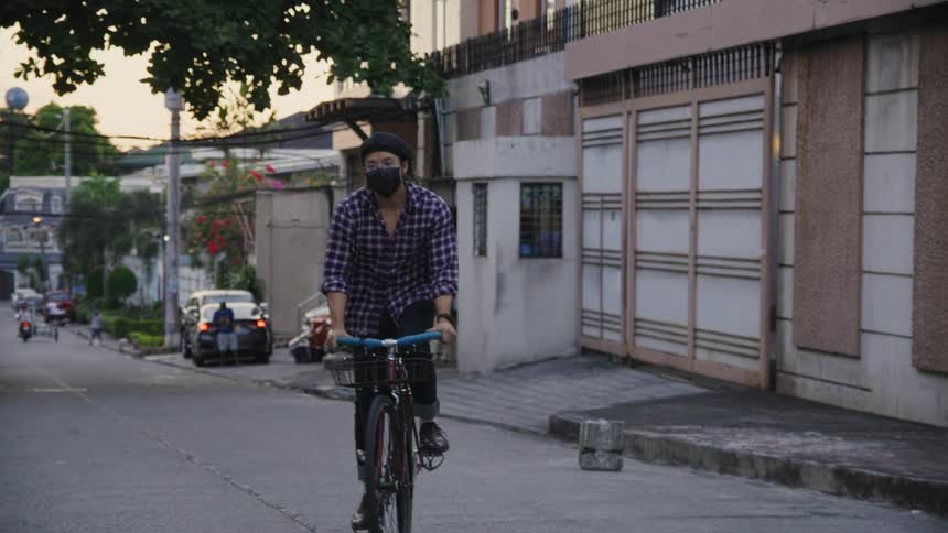 Man wearing mask pedals along street past apartment building