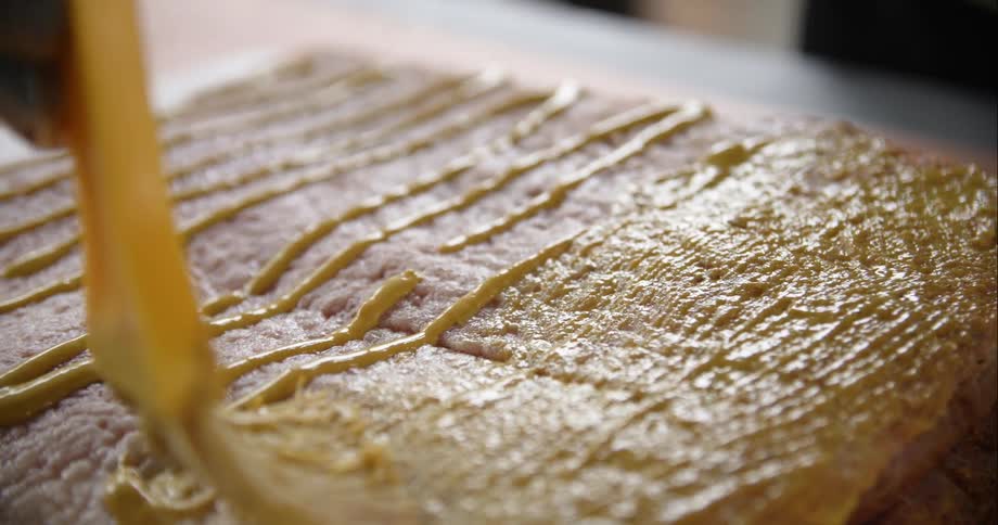 A view of a person brushing mustard on a piece of meat