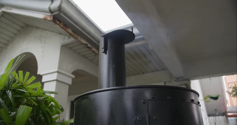 Smoke rises from a large meat smoker as food is cooked in a backyard