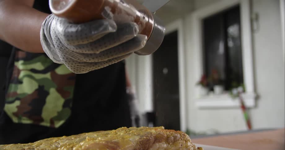 A person with gloves sprinkling seasoning on a piece of meat on a cutting board on a table