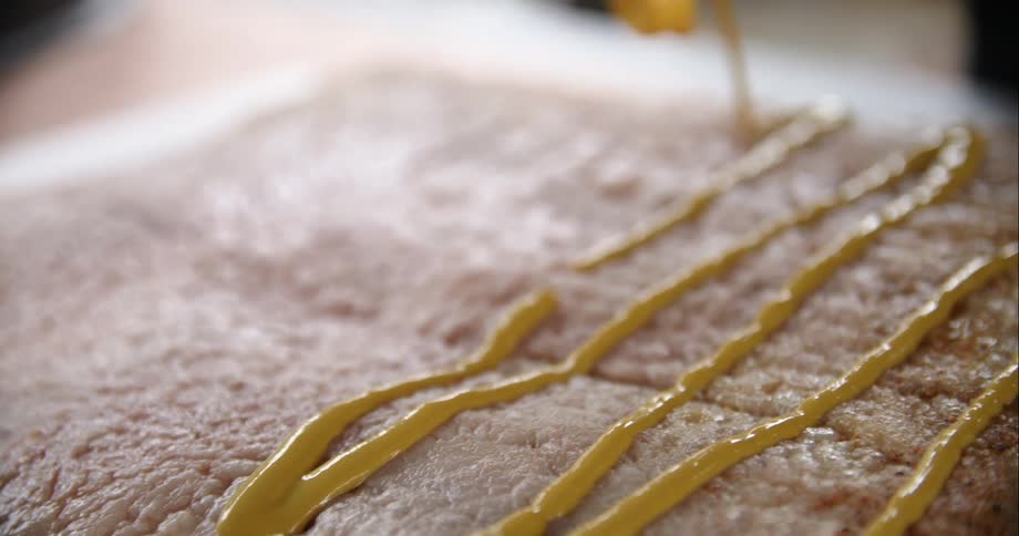 Mustard being placed on a piece of meat on a cutting board on a table