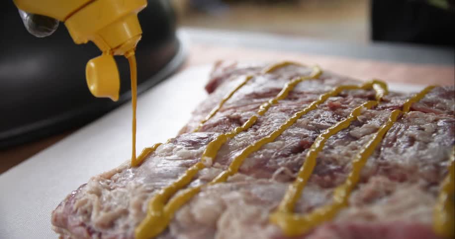 Mustard being put on meat before cooking