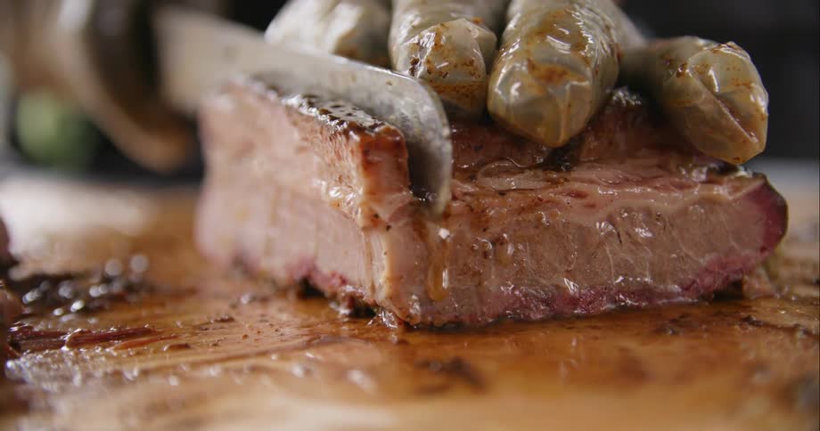 Chef wearing latex gloves cutting a tender piece of meat over a wooden table with a sharp kitchen knife