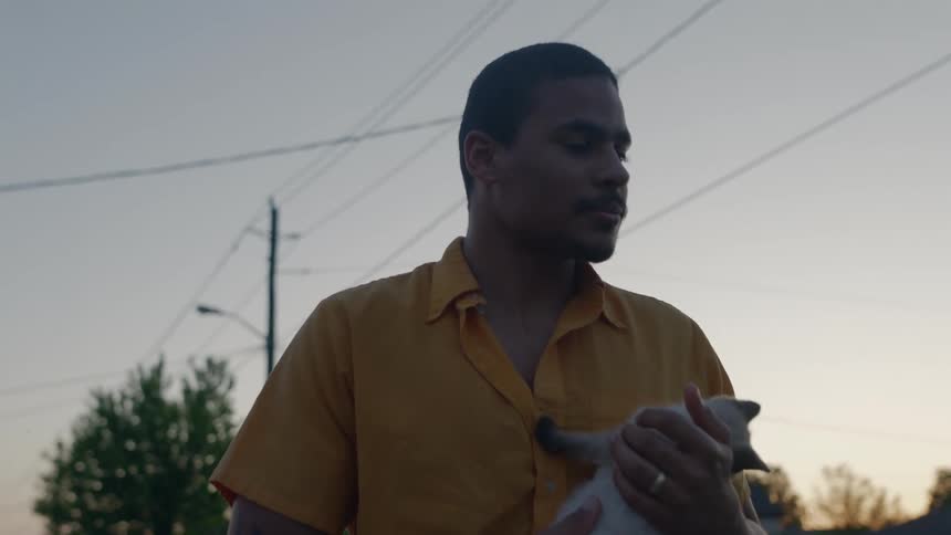 A man holds his kitten while standing outside his house