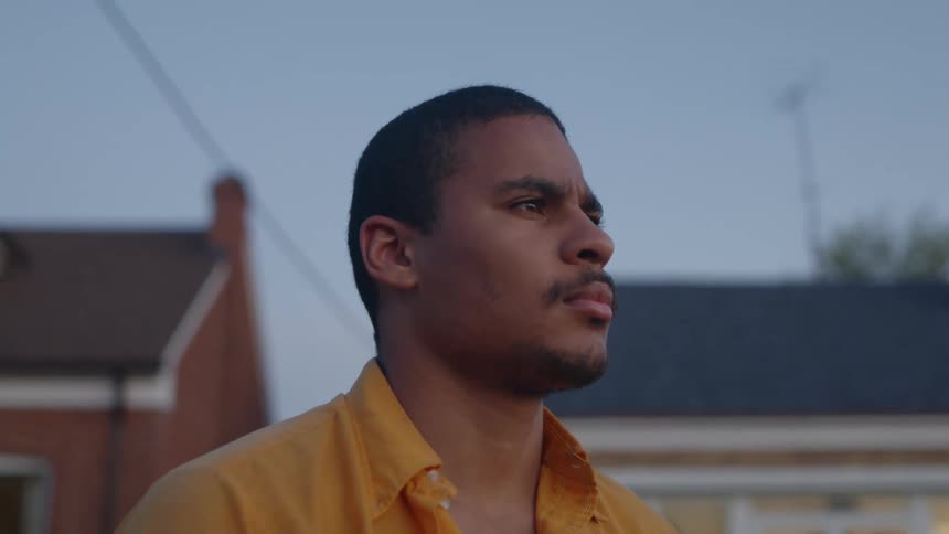 Man with orange shirt looks around in the neighbourhood at dusk