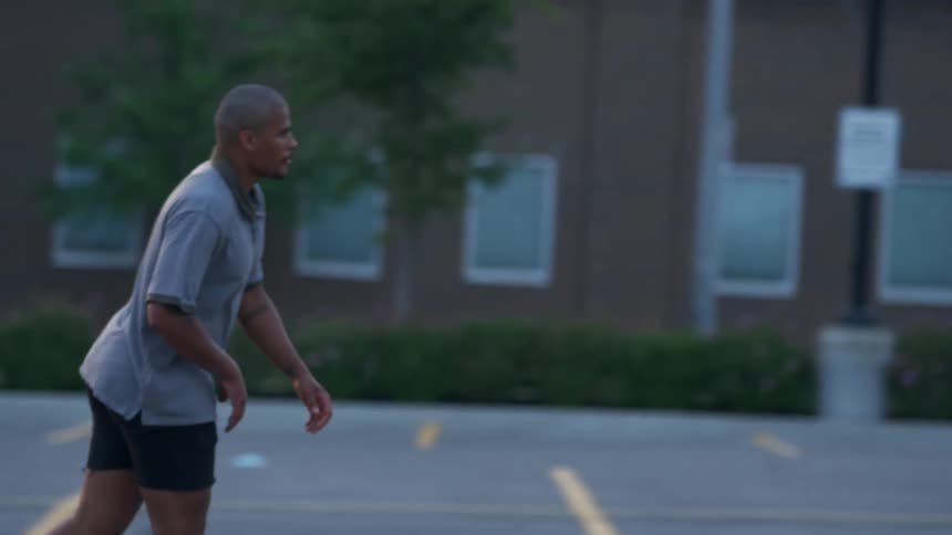 A man skateboards through an empty parking lot during the day
