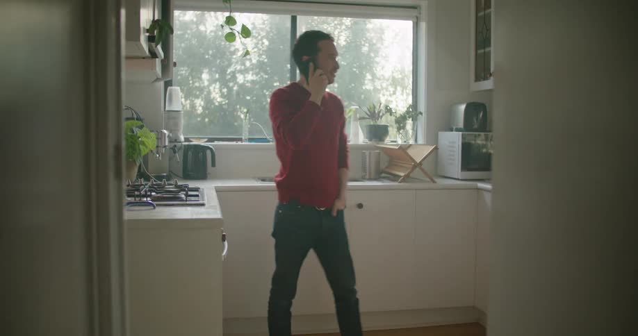 A man walking around in a kitchen talking on a phone