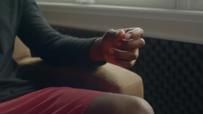 A person wearing shorts and a long sleeve shirt sits in a chair while rubbing their fingers together