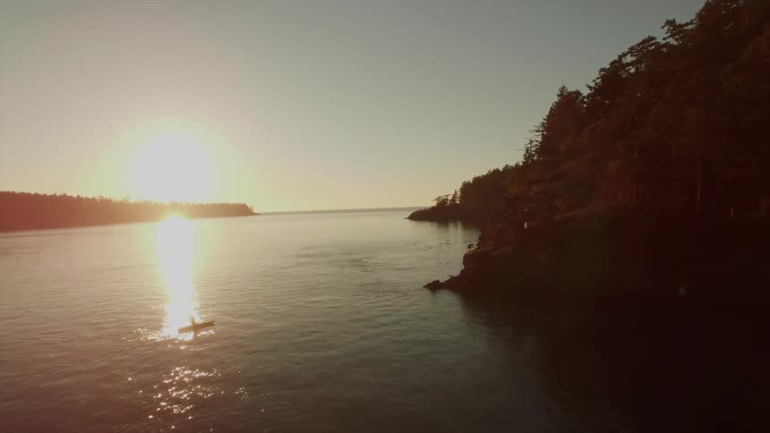 The sun is setting in the distance as a boat travels in the water