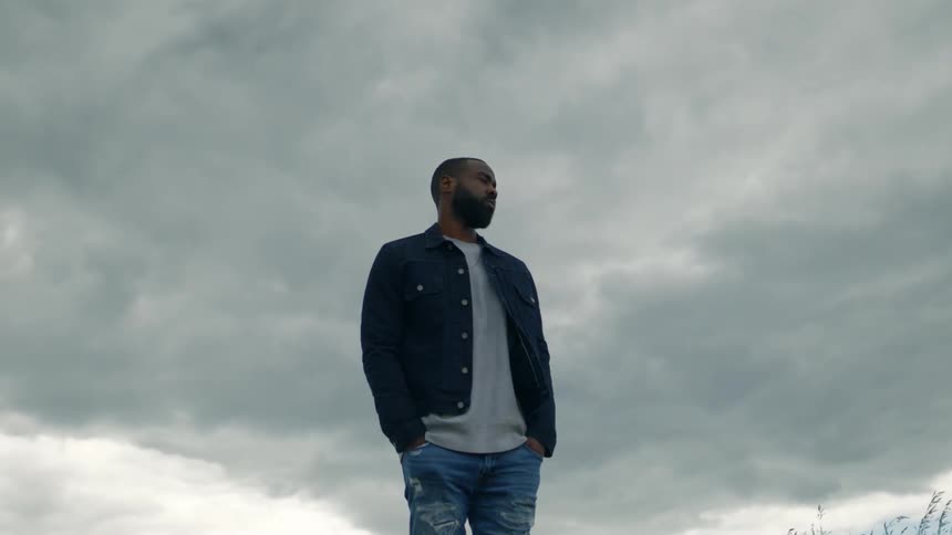 A man stands under the cloudy sky