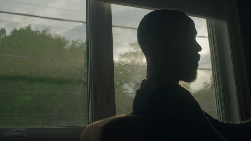 Silhouette of a young bearded man drinking a hot beverage while sitting in a room in the morning