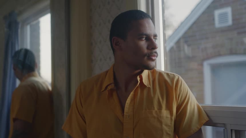 Man wearing yellow shirt looking out the window at home in the morning