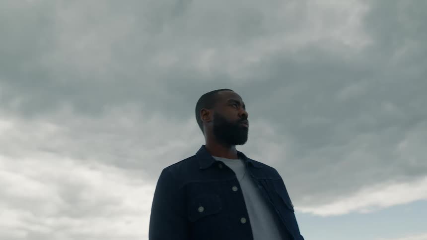 Man stands in field under heavily clouded sky with city skyline in distance