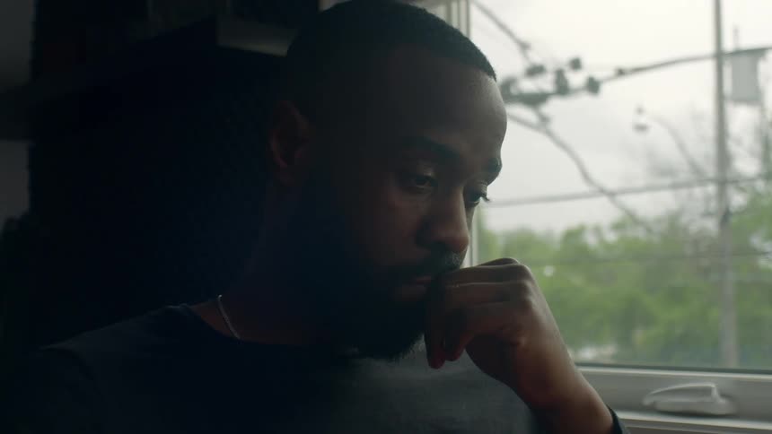 A man sits resting by the window of his home