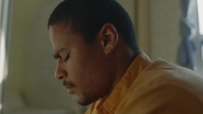 A man with a thin mustache sits indoors with his eyes closed in contemplation