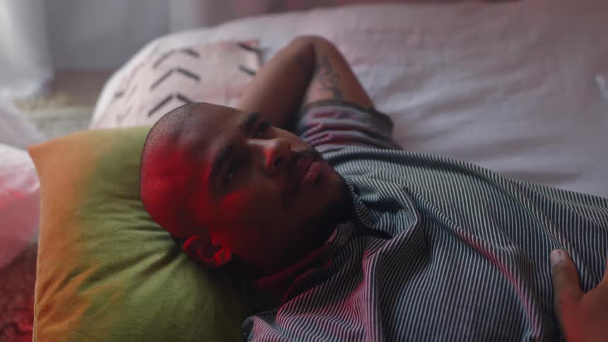 A man in a room laying on a bed and a pillow with a wall in the background