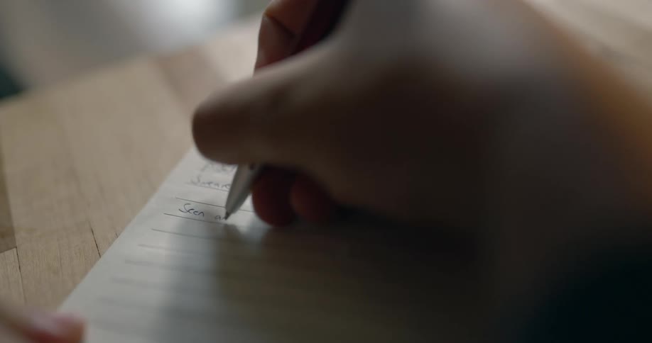 A man writes in a small notebook while sitting at a wood table