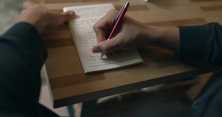 A person sits at a desk in a classroom and takes notes