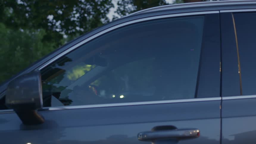 A woman inside a car parked in a neighborhood puts on the seat belt before driving away