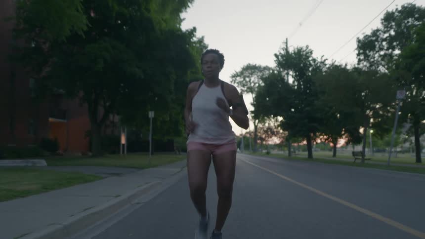 A woman down the middle of the street past a neighborhood park