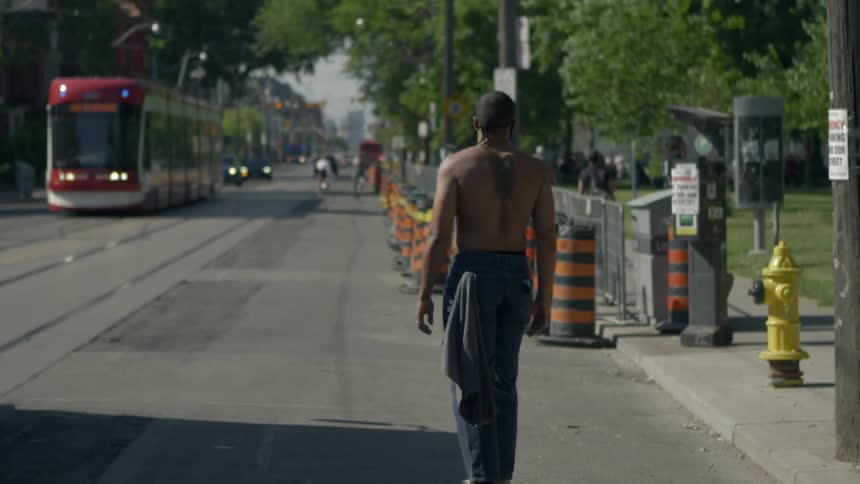 A shirtless male rides his skateboard along a city street near a public park