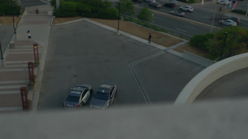 A man is looking at two parked police vehicles from the roof