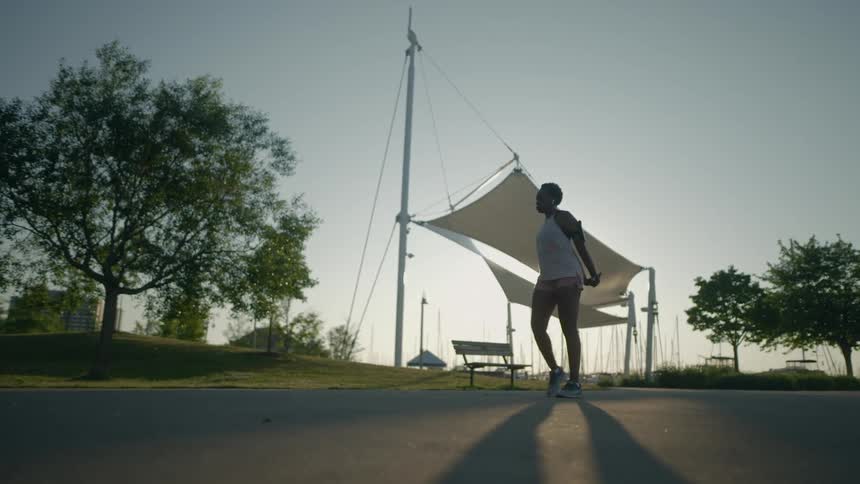 A female runner comes to a stop near a public park in order to pause to stretch