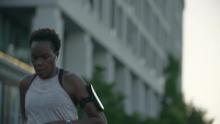 A female runner listens to music on her air pods while her smartphone is strapped to her arm