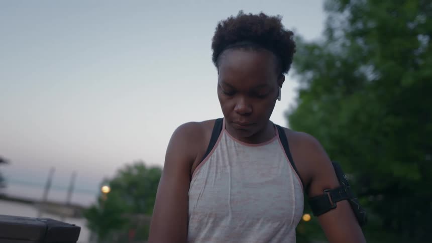 A woman is outdoors in a park in the early morning stretching before going for a jog