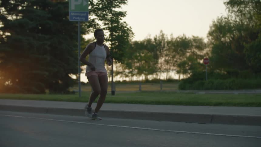 A woman jogging on the street past an empty park at sunset