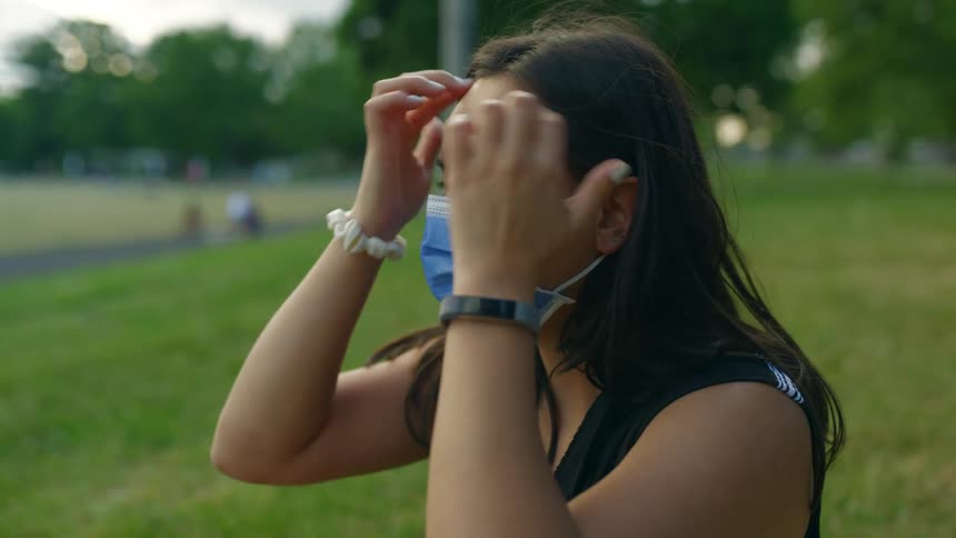 A woman in a park putting on a face mask