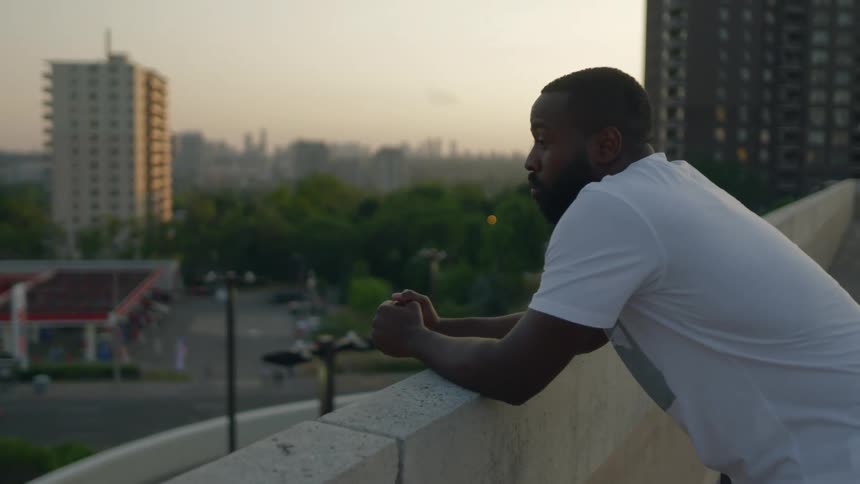 A man is leaning on the ledge of the roof looking at the neighborhood
