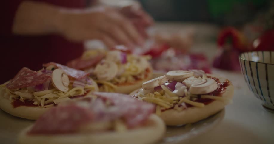 Person preparing small pizzas with mushroom and pepperoni at home